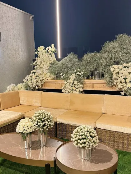 A chic outdoor lounge area with a beige velvet sofa, surrounded by an abundance of white roses and baby's breath.