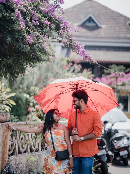 A romantic moment under a red umbrella on a colorful street in Goa, with bougainvillea flowers adding to the charm.