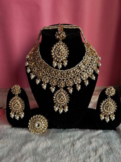 Where elegance meets art. This is a complete Kundan set with a necklace, earrings, maang tikka, and a matching ring, all in a beautiful golden finish with pearls.