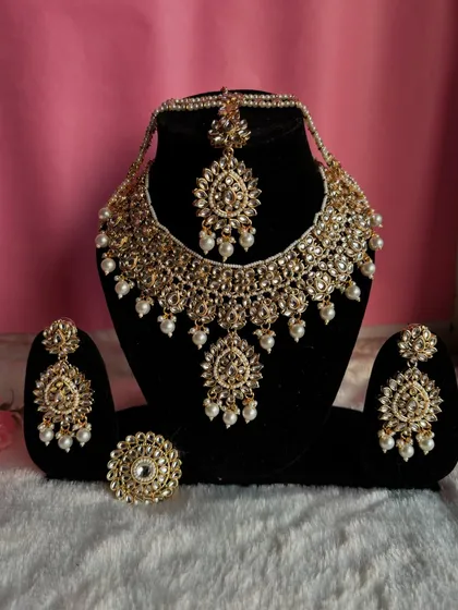 A classic gold-plated Kundan set with pearl drops. This complete set includes a necklace, earrings, maang tikka, and a matching ring.