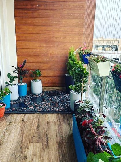A stylish balcony corner featuring a mix of planters on the floor and railing, with a pebble bed adding a decorative touch.