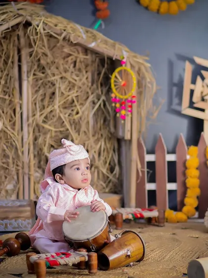 This little one is ready to celebrate Lohri, sitting with a small dhol. The festive Punjabi village theme creates a warm and celebratory atmosphere.