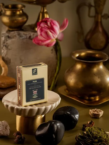 A moody and elegant composition for Zeva's 'Nak' soap. The dark background, brass artifacts, and single pink tulip create a sense of mystery and sophistication, positioning the product as a premium offering.