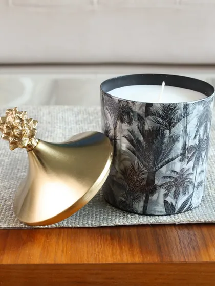 A close-up of our Monochrome Forest scented candle. The black and white palm print and gold pineapple lid create a look of pure tropical sophistication.