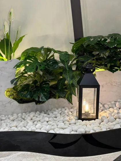 The combination of textured Monstera leaves, smooth white pebbles, and the warm light from a lantern creates a multi-sensory experience in this small but impactful green corner.