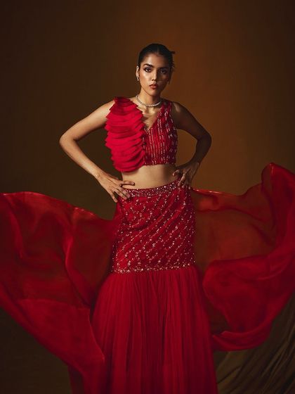 A dramatic, wide-angle shot of a red lehenga from Label Japji Arora, with the organza dupatta creating a sense of movement.
