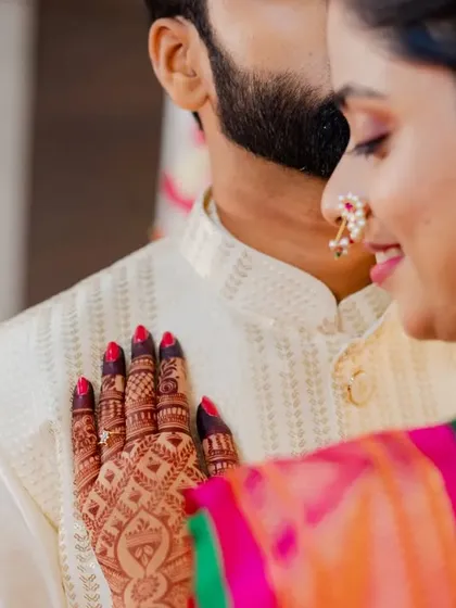 A detailed shot of the bride's hand on her fiancé's chest, showing off her intricate mehendi and the traditional nose ring (nath).