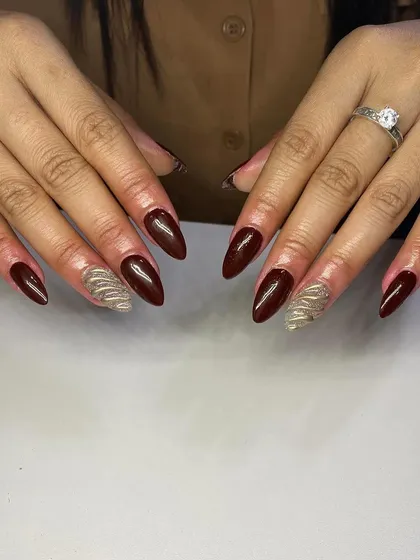 A sophisticated combination of deep red and gold. These almond-shaped extensions have accent nails with a textured gold design.