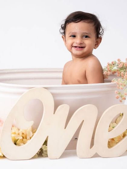 The "One" sign and a happy baby in a tub. This is a classic shot from a cake smash and splash session, beautifully concluding the first birthday celebration.