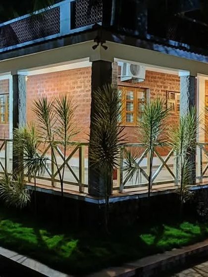 The "Grid in the Grove" farmhouse at night. The lighting design creates a dramatic and inviting ambiance, highlighting the rustic texture of the laterite block walls and the traditional form of the building.