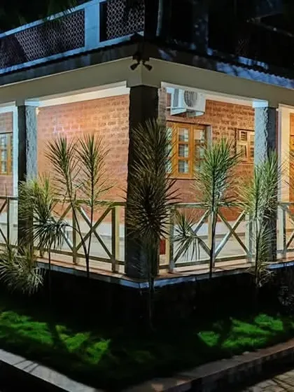 The "Grid in the Grove" farmhouse at night. The lighting design creates a dramatic and inviting ambiance, highlighting the rustic texture of the laterite block walls and the traditional form of the building.