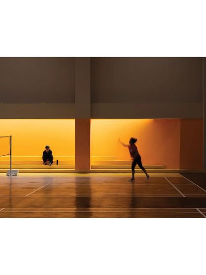 The badminton court at the 'Meraki' clubhouse is designed with warm, indirect lighting to create a pleasant and functional environment for players.