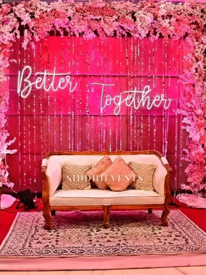 A vibrant pink floral arch frames a 'Better Together' neon sign, creating a bold and romantic photo backdrop for a reception or sangeet night.