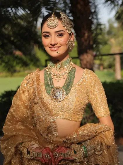 A happy bride glowing in her golden ensemble. The styling focuses on the stunning contrast between the gold outfit and the vibrant green of the heritage jewelry.