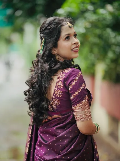 A lovely shot from the back, showcasing the bride's long, flowing curls and the beautiful embroidery on her purple saree blouse.