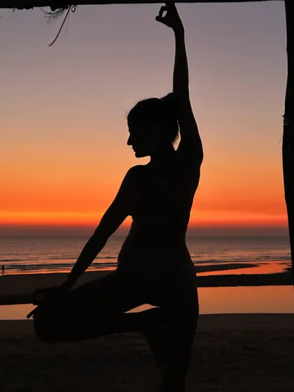 A silhouette against a fiery Goan sunset. This Tree Pose variation, framed by a beach shack, captures the magical moment where light meets dark, a time of transition and quiet beauty.