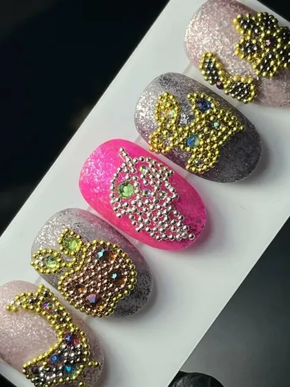 Magical crystal nail art. This design uses tiny metallic beads to create intricate patterns like pineapples and grapes over a glittery base.