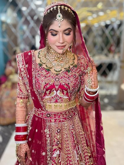 A full-length shot of the bride, showing how her makeup and hair complement her stunning red lehenga with peacock embroidery.