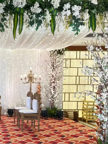 This angle of the white mandap highlights the beautiful textures, from the patterned carpet to the delicate blossoms and the soft glow of the fairy light curtain.