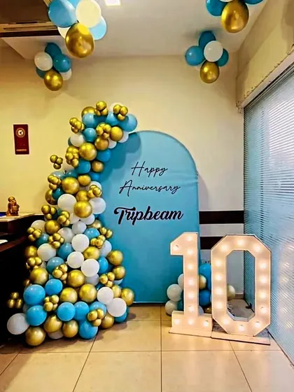 A corporate anniversary celebration for Tripbeam. This setup features a blue and gold balloon cascade against a custom arched backdrop, along with a light-up number '10'.