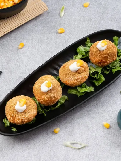 Crispy cheese corn balls arranged on a modern black platter. The composition is clean and elegant, elevating a simple snack into something more special.