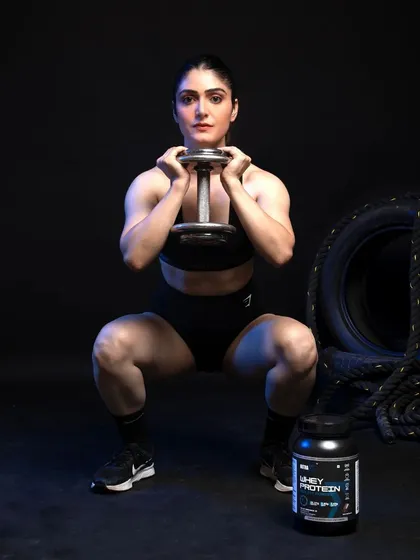 An action shot demonstrating a lifestyle application of the product. The female model is mid-squat, associating the supplement with strength and performance. The product is placed clearly in the foreground, ensuring it remains the focus even during a dynamic scene.