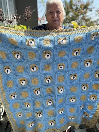 A variation of our bear-themed blanket, this time in a beautiful blue and gold color scheme, held up by Dadi in her garden.