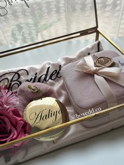 A close-up of the personalized bridesmaid gift in a glass box, featuring a custom mirror with the name 'Aaliya' in calligraphy.
