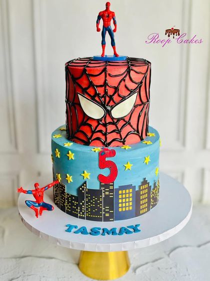 A heroic two-tier Spider-Man cake for a 5th birthday. The top tier features Spidey's iconic mask, while the bottom shows a city skyline, ready for action.