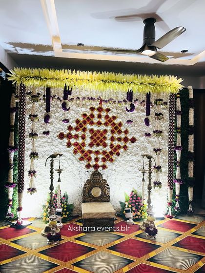 A close-up of a Haldi or Sreemantham backdrop, showing the intricate geometric pattern made with red and white flowers. The decor is complemented by hanging floral tassels.