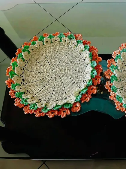 A bright and cheerful floral placemat with layers of orange, green, and cream petals. This piece is sure to brighten up any space.