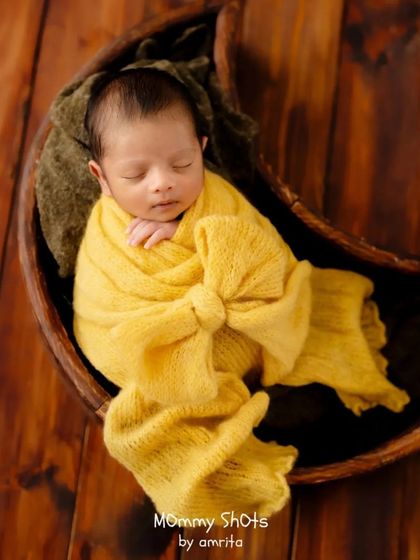A newborn wrapped in a vibrant yellow bow wrap, nestled in a wooden moon prop.