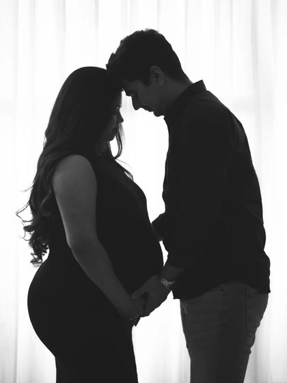 A classic black and white silhouette. This intimate pose of a couple touching foreheads against a bright window creates a timeless and romantic image.