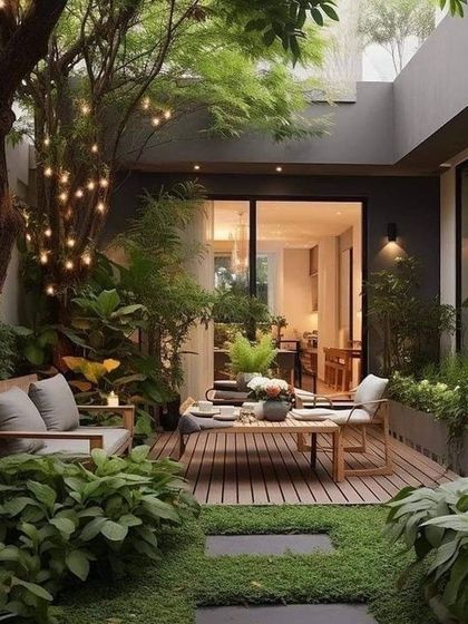 An intimate and magical courtyard garden. We used a combination of wooden decking for the dining area, stepping stones on grass, and lush surrounding greenery with string lights in the tree to create a cozy and enchanting atmosphere.