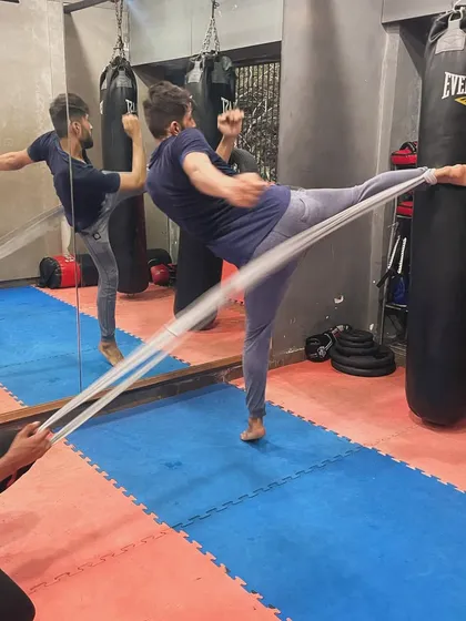A client works on his kicking flexibility and power using a resistance band. This exercise helps increase the height and speed of his kicks, essential for martial arts training.