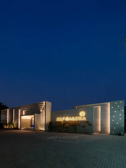 A wide-angle view of the HLP Galleria, capturing the full scale of its modern architectural design against the evening sky. The composition emphasizes the building's clean lines and minimalist elegance.