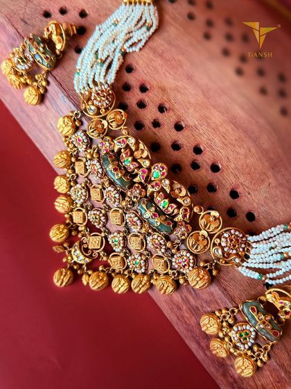 This gold choker combines intricate detailing with regal meenakari hues of red and green. The delicate pearl strings add a touch of softness to the grand design.
