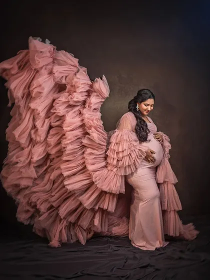 A side profile showcasing the beautiful cascade of ruffles on our pink maternity gown. This pose elegantly highlights the baby bump.