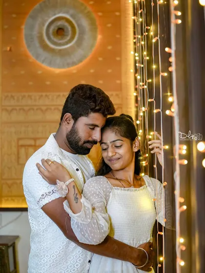 A sweet, intimate moment for a couple in all-white, with the warm glow of indoor lights creating a cozy feel.