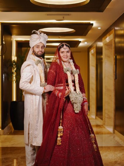 A full-length portrait of the couple in a hotel corridor. Their traditional red and white wedding outfits create a striking contrast against the modern interior.
