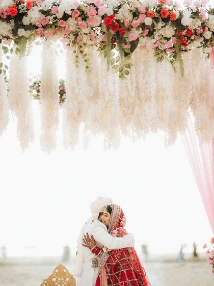 A warm embrace under the floral mandap. This shot shows how the makeup looks beautiful and natural in a bright, outdoor setting.