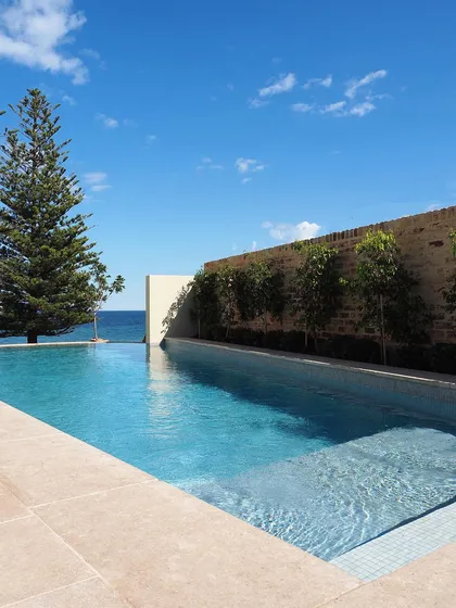 A view from the corner of the infinity pool, showing how the water meets the sky. A line of trees planted against a stone wall provides privacy without blocking the beautiful ocean view.
