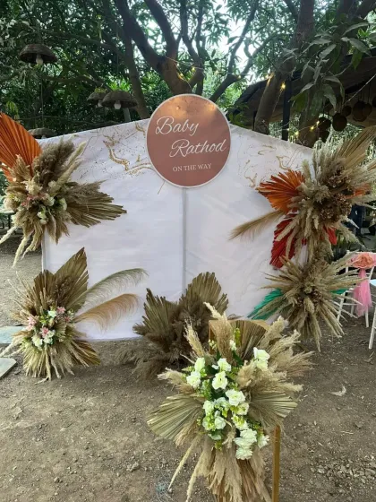 An outdoor baby shower setup with a tented backdrop and arrangements of pampas grass and dried florals for a natural, boho feel.