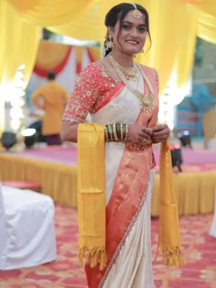 A full view of a stunning Telugu bride in her pre-pleated saree. The drape is elegant and clean, allowing the beauty of the saree and the bride's joy to shine through at her wedding venue.