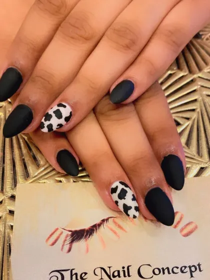 Show off your fun side with this matte animal print nail art. This set combines solid matte black nails with accent nails featuring a hand-painted black and white cow print on a trendy almond shape.