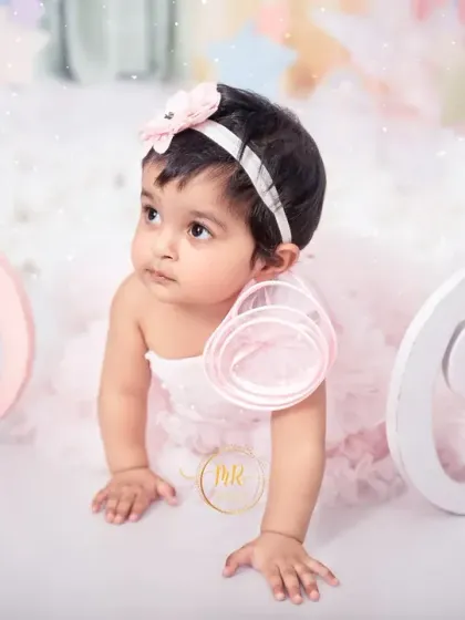 A curious baby girl crawling amidst fluffy clouds and large "One" letters during her magical, pastel-themed first birthday shoot.
