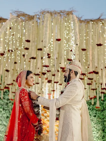 A beautiful candid moment of the couple under the dense floral canopy of the Kalpavṛkṣa mandap.