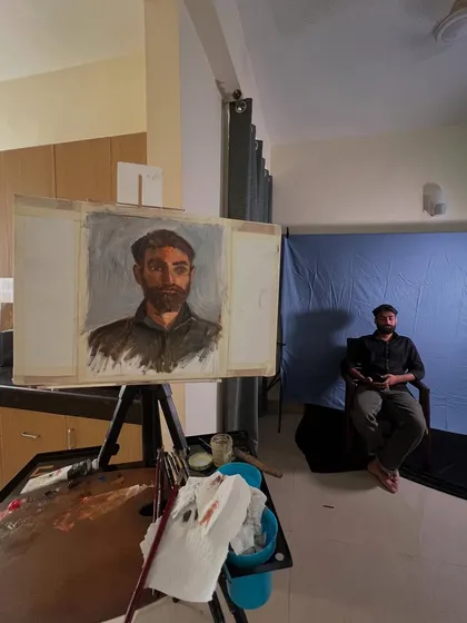 The complete setup for Rishabh's portrait session. You can see the canvas, my palette with mixed Gamblin oil colors, and Rishabh posing against the backdrop.