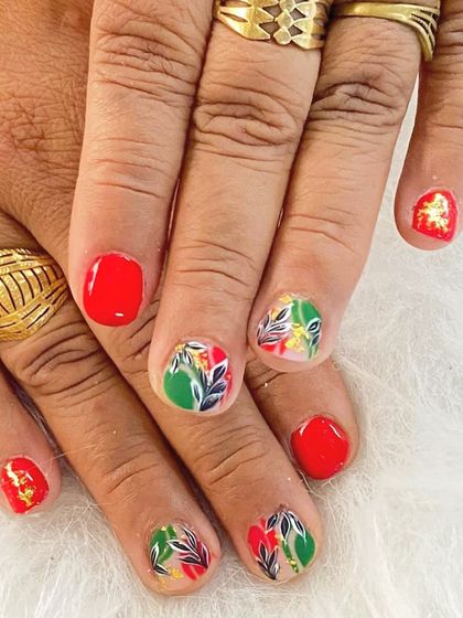 A vibrant and artistic design on short nails, featuring a mix of red and green with a leafy pattern and gold foil accents.