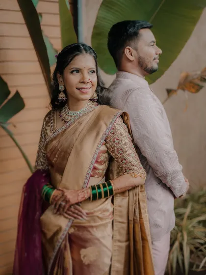 A classic pose from a Maharashtrian engagement shoot. The bride, adorned in a beautiful saree and jewelry, looks away with a gentle smile while her partner stands behind her, creating a feeling of quiet confidence and togetherness.